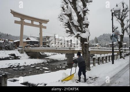 28.12.2017, Takayama, Gifu, Giappone, Asia, un uomo spalanca la neve su una strada accanto al ponte Miyamae Bashi, a un'estremità della quale si trova una grande porta torii Foto Stock