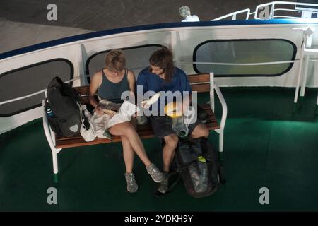 Due giovani backpackers sono seduti su una panchina del traghetto e mangiano qualcosa di notte, Bari, Puglia, Italia Foto Stock