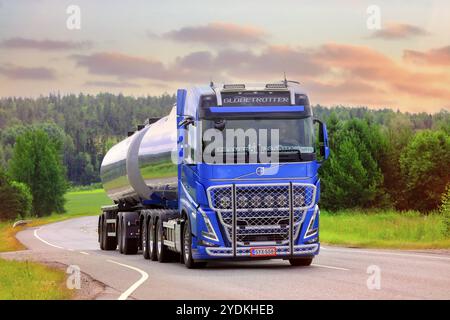 Nuovo camion cisterna blu Volvo FH540 di Transport Sjoman Oy Ab su strada al tramonto estivo. Immagine composita. Salo, Finlandia. 24 giugno 2021 Foto Stock