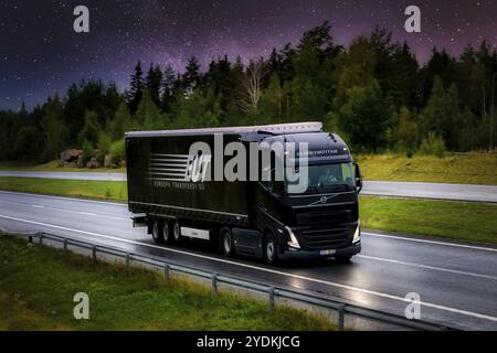 Nuovo semirimorchio Volvo FH nero Euroopa Transpordi OU che trasporta merci in autostrada sotto il cielo stellato di notte. Immagine composita. Finlandia, 2021 Foto Stock