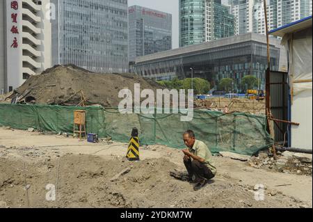 16.08.2012, Pechino, Cina, Asia, Un uomo accovacciato di fronte a un cantiere edile nel centro finanziario della capitale cinese, Asia Foto Stock