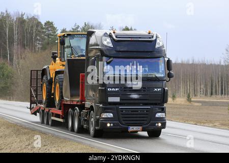 SALO, FINLANDIA, 13 APRILE 2017: Il DAF XF semi nero trasporta la pala gommata Volvo su un rimorchio a collo d'oca lungo l'autostrada rurale in una giornata nuvolosa con neve Foto Stock