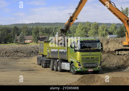 L'escavatore cingolato carica il terreno su un rimorchio a cassette Volvo FH16 verde in un giorno d'estate. Copia spazio rimanente. Salo, Finlandia. 27 agosto 2022 Foto Stock