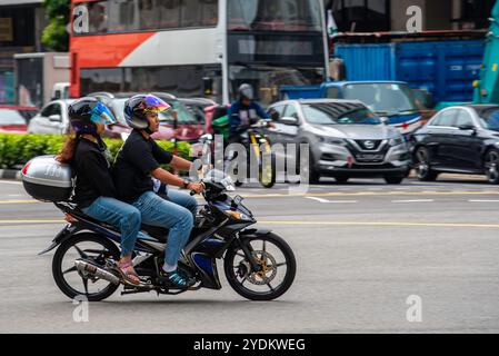 Trainare persone di Singapore in sella a Pillion indossando magliette e caschi aperti su una moto o uno scooter nel traffico di Singapore Foto Stock