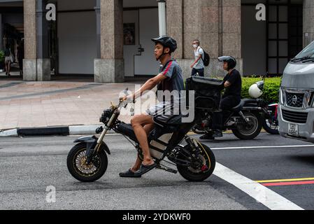 Una persona di Singapore che guida una bici elettrica elettrica o uno scooter si è fermata in un incrocio nel traffico di Singapore Foto Stock