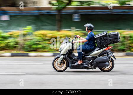 Una persona di Singapore che utilizza il proprio telefono cellulare mentre guida su uno scooter nel traffico di Singapore Foto Stock