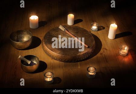 Il set di tamburello sciamano, ciotola tibetana e candele in una stanza buia Foto Stock