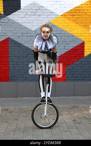 Una ragazza clown in abiti da circo che si esibisce con un unicycle all'aperto Foto Stock