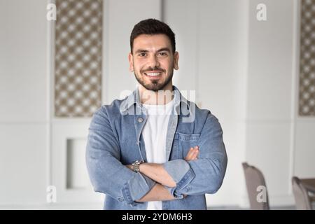 Felice affascinante uomo d'affari mediorientale in piedi al chiuso con le mani incrociate Foto Stock
