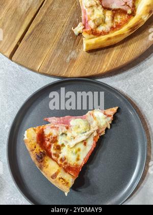 Fetta di pizza appena cotta su un piatto grigio. Pizza fatta in casa con prosciutto, carne di pollo e formaggio Dor Blue. Primo piano. Foto Stock