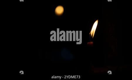 Una candela luminosa brucia brillantemente su uno sfondo nero. Le candele bruciano di notte. Candela bianca che brucia al buio con attenzione su una singola candela in t Foto Stock