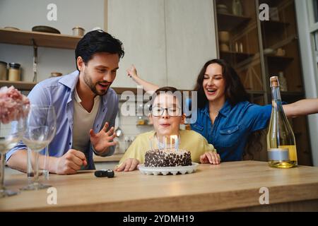 Festeggiamo il compleanno dei bambini con torta, candele e genitori gioiosi a casa Foto Stock