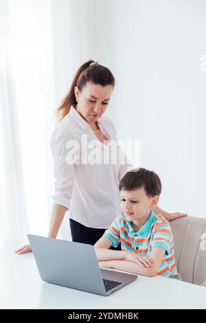 Donna gentilmente cortese che mostra a uno scolaro al tavolo un portatile Foto Stock