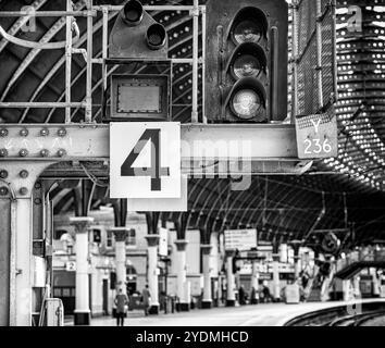 Una luce segnaletica e un cartello con il numero di piattaforma si trovano su un cavalletto sopra la piattaforma di una stazione ferroviaria. Il passeggero si trova sulla piattaforma e su una passerella e decorata c Foto Stock