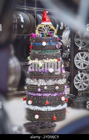 Un albero di Natale unico realizzato con pneumatici, decorato con ornamenti e un cappello di Babbo Natale, esposto in un'officina di riparazione auto Foto Stock