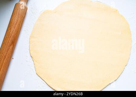 Impasto a forma di cerchio arrotolato per pizza o torta su un tavolo leggero con un mattarello di legno. Foto di alta qualità Foto Stock