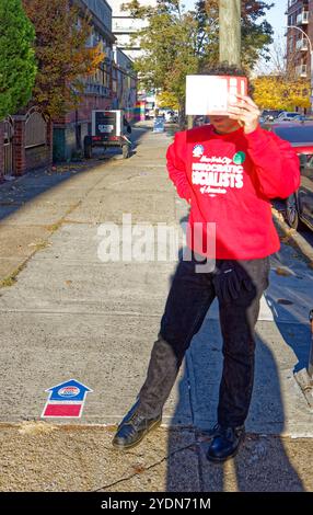 Proteggendo gli occhi dal sole del mattino presto, un volontario del Partito Socialista Democratico di New York attende gli elettori nel sito di voto anticipato, facendo una campagna per le proposte di voto di New York. Foto Stock