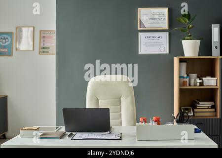 Ufficio moderno con scrivania organizzata con laptop e articoli da ufficio, completato da ripiani ordinati e certificati a parete per creare un ambiente professionale Foto Stock