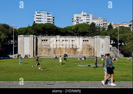 Persone che si godono un pomeriggio vivace alla fonte luminosa di Lisbona, con bambini che giocano a calcio e amici che si rilassano sull'erba Foto Stock