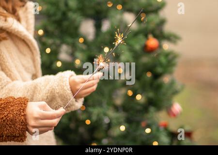 Qualcuno che tiene con gioia uno sparkler mentre è circondato da decorazioni festose e da un albero di Natale luminoso, che esalta lo spirito natalizio. Foto Stock