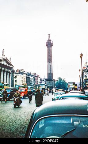 Una vista del 1957 del Nelson's Pillar in o'Connell Street, Dublino, Irlanda, con ciclisti e auto che condividono la strada, e auto parcheggiate sulla sinistra fuori dal Clery's Department Store. Nelson’s Pillar è stato eretto nel 1809 e fatto esplodere da un repubblicano irlandese nel 1966. Foto Stock