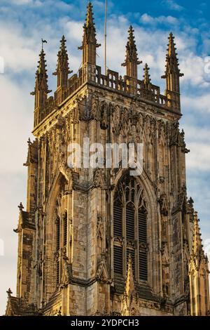 Una vista ravvicinata della sezione superiore di un'alta torre cattedrale in pietra con intricati dettagli gotici e una grande finestra ad arco. La pietra è un mix Foto Stock