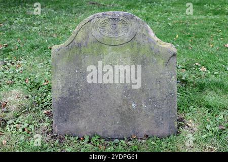 Un primo piano di una lapide molto vecchia. La pietra è vuota tranne che per un disegno nella parte superiore. La pietra risale al XVIII o XIX secolo. L'erba lo circonda. Foto Stock