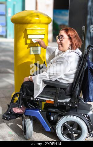 Utente donna in sedia a rotelle sorridente durante l'utilizzo della cassetta postale pubblica Foto Stock