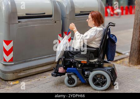 Donna in sedia a rotelle che utilizza il cestino pubblico per il riciclaggio Foto Stock