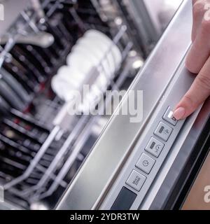 La mano della donna si accende in lavastoviglie per lavare i piatti. Elettrodomestici incorporati in cucina Foto Stock