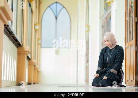 L'immagine di una donna musulmana asiatica nella religione islamica in hijab di colore crema. Pregava in una bella moschea per rispetto verso Dio. Foto Stock