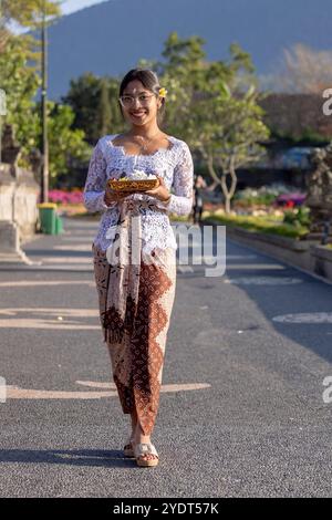 Bali, Indonesia - 25 settembre 2024 - famiglia balinese vestita con abiti tradizionali, in piedi all'ingresso di un tempio, che offre preghiere e onorificenze Foto Stock