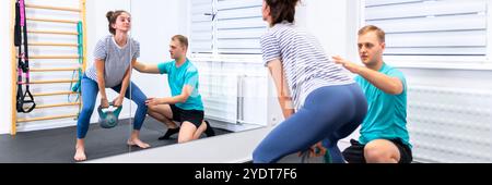 Donna con mal di schiena in terapia fisica. Fisioterapista che fa esercizio con paziente femmina che fa esercizi di mobilità della schiena usando un kettlebell. Foto Stock
