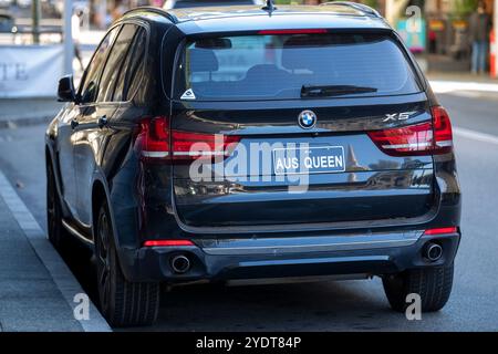 BMW X5 nera parcheggiata su una strada cittadina, con una targa personalizzata con la scritta "AUS QUEEN" visibile sul retro del veicolo. Foto Stock