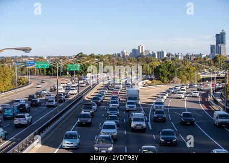 Una trafficata superstrada a Perth, Australia, piena di veicoli nel traffico pomeridiano, con cartelli direzionali verdi e alti edifici. Foto Stock
