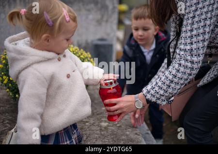 Madre e figli che illuminano una candela su una tomba Foto Stock