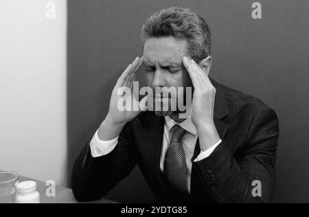 Uomo stressato con mal di testa. Un uomo d'affari stanco lavora straordinari e ha mal di testa. Uomo con notebook sul posto di lavoro, soffre di mal di testa. Emicrania da Foto Stock