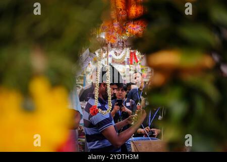 Singapore 2019 luglio 19 - uomo indiano che dimostra come fare ghirlande di fiori freschi ai turisti in negozio a Little India, girato attraverso ghirlande di fiori Foto Stock