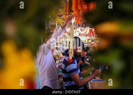 Singapore 2019 luglio 19 - uomo indiano che dimostra come fare ghirlande di fiori freschi ai turisti in negozio a Little India, girato attraverso ghirlande di fiori Foto Stock