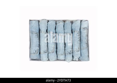 Collezione di jeans in denim blu chiaro ripiegati ordinatamente in scatola di stoccaggio, cassetto dell'abbigliamento organizzato con pantaloni arrotolati, armadio in stile Marie Kondo Foto Stock