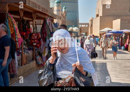 Khiva, Uzbekistan; settembre, 21,2024: Un'anziana donna uzbeka che indossa un velo tradizionale, impegnata in una conversazione telefonica Foto Stock