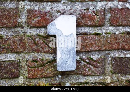 Casa numero uno su un muro. La vernice bianca sul numero si sta staccando Foto Stock