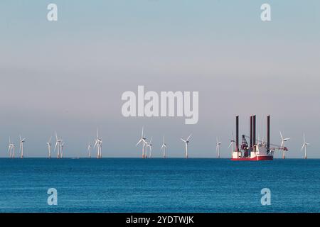 Sollevare la nave di installazione delle turbine eoliche in mare, con il parco eolico sullo sfondo e il cielo colorato. Foto Stock