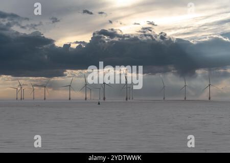 Le turbine eoliche offshore si estendono nell'oceano con un cielo spettacolare e acque calme. Foto Stock