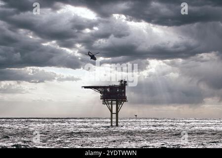 Elicottero che vola verso la piattaforma petrolifera offshore in mare per l'atterraggio, con nuvole nel cielo e mare blu. Foto Stock