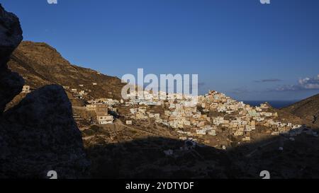 Colline immerse nell'oscurità con l'ultimo villaggio illuminato, accompagnate da profonde ombre di rocce, colorato villaggio di montagna, luce mattutina, Olymbos, Karp Foto Stock