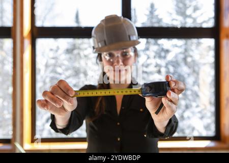 Attenzione selettiva al metro sulle mani della donna, è un'ispettore edile che sorride e indossa indumenti di sicurezza durante l'ispezione degli interni della casa Foto Stock