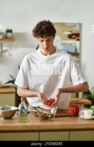 Un bel giovane in una cucina moderna prepara con cura un'insalata fresca, abbracciando una vita sana. Foto Stock