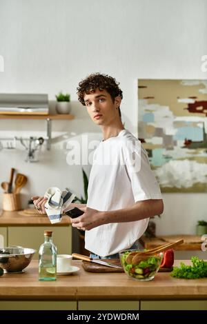 Un bel giovane con i capelli ricci prepara sapientemente un'insalata fresca nella sua cucina contemporanea. Foto Stock