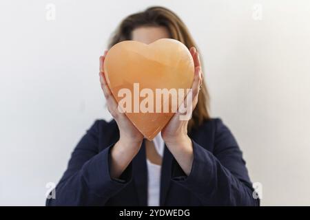 Una donna di successo viene visto dalla parte anteriore contro uno sfondo bianco, tenendo a forma di cuore in pietra minerale sul suo viso utilizzati in alternativa la salute th Foto Stock